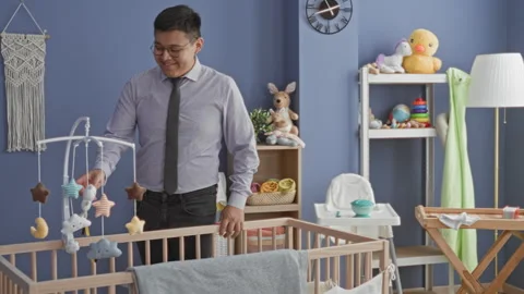 Man touching mobile at crib in studio blue nursery, smiling while checking .. Stock Footage 337357347