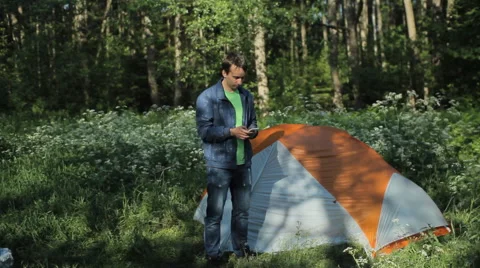 The man is touching the phone next to the tent. Early morning in the forest Stock Footage 64326826