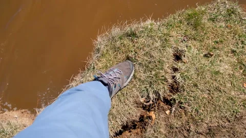Man touching sandy crashing ground by leg in dirty sneakers on river bank. Stock Footage 311869148
