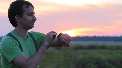 Man touching smart clock on the background of beautiful sunset sky Stock Footage 64777230