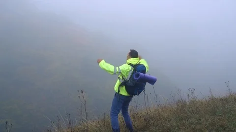 Man tourist with backpack climbed the mountain and screams with joy waving his Stock Footage 95674417