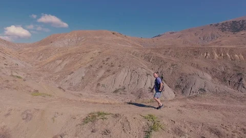 A man tourist with a backpack climbs the path to the mountains against the blue Stock Footage 97858138
