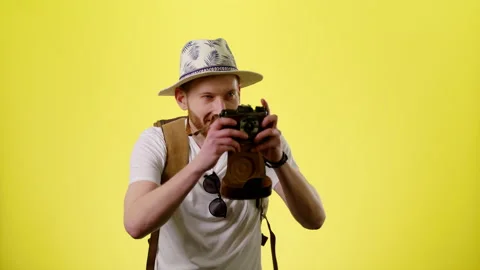 Man With Tourist Backpack, Hat And Camera Taking Photo On The Yellow Background Stock Footage 170183121
