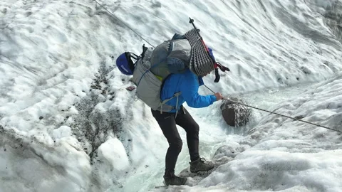 Man with a tourist backpack jumps over a turbulent stream in a glacier 스톡 동영상 158670543