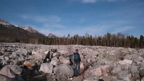 Man tourist with backpack looking for way among rocks of landslide in mountains. Stock Footage 229620057