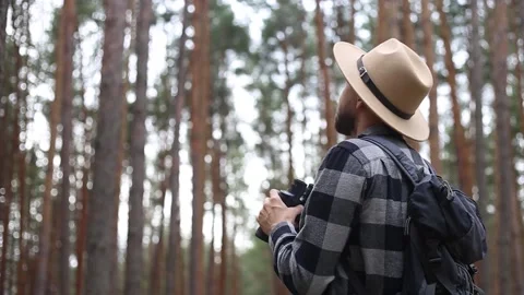 Man tourist with a backpack looks through binoculars while hiking in the forest Stock Footage 149946594