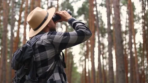 Man tourist with a backpack looks through binoculars while hiking in the forest Video stock 149946598