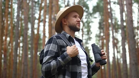 Man tourist with a backpack looks through binoculars while hiking in the forest Stock Footage 149946601