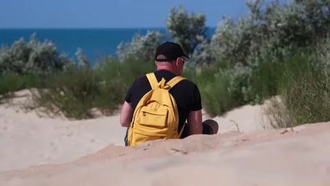 Man tourist with backpack sits on sand beach dune looking at amazing sea view Stock Footage 201428371