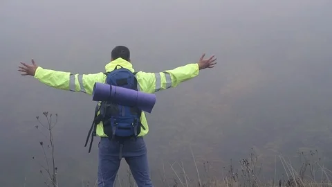 Man tourist with backpack stands on the edge of the mountain in the fog waving Stock Footage 95650899