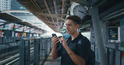 Man tourist with backpack using mobile phone while waiting for skytrain at metro Stock Footage 255288984