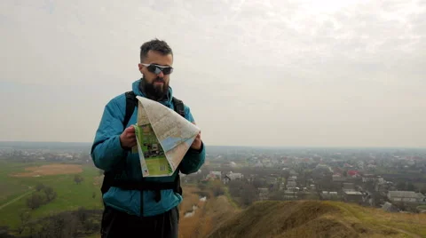 Man tourist in a blue jacket with a backpack looking on the map Stock Footage 62399199