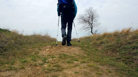 Man tourist in a blue jacket with a backpack and trekking poles walks outdoor Stock Footage 62399368