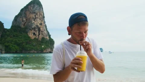 Man tourist drinking yellow mango smoothie in plastic cup with a straw on Stock Footage 280941017