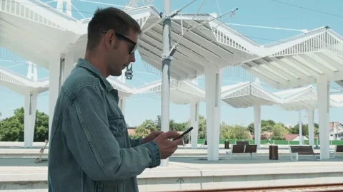 Man tourist with smartphone looking at the train schedule at railway station Stock Footage 286358948