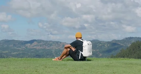 Man tourist with white backpack sitting on top of mountain looking at view. Stock Footage 260845873