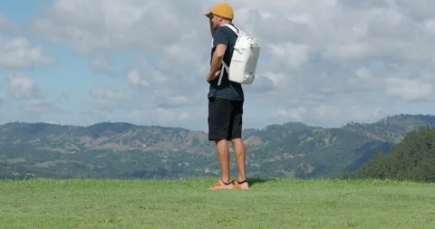 Man tourist with white backpack standing on edge of mountain looking at view. Stock Footage 260845828