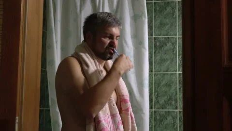 A man with a towel around his neck is brushing his teeth and gesticulating wi Stock-Footage 112795168
