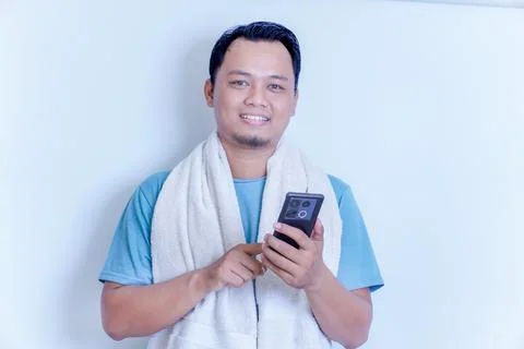 A man in a towel smiles while using his smartphone, enjoying a relaxed moment Stock Photos