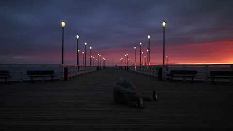 Man In Tracksuit and Protective Face Mask Stretching on a Seaside Pier at Dusk - Stock Footage 130738182