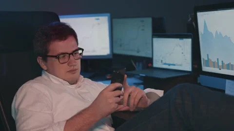 Man trader with phone and computers with stock market graphs, home office 스톡 동영상 144344404