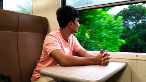 Man in a train sitting by a window, watching beauty of nature on mountain route 動画素材 250200157