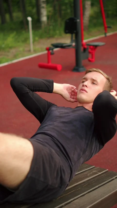 Man training abs on a bench on an outdoor fitness bench. Young man performi.. Video stock 341728533
