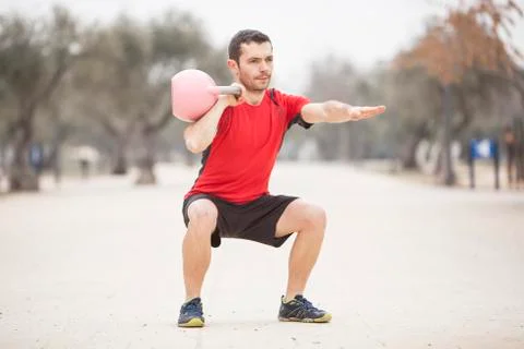 Man training with kettle bell with extended arm and in squat Stock Photos