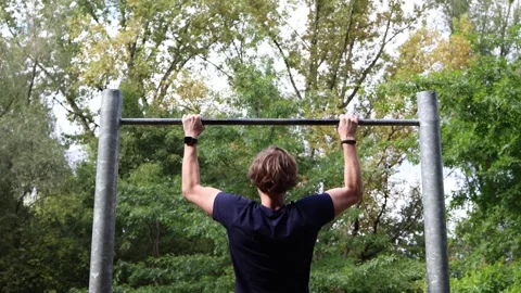 Man training outdoors doing pull ups on bar in park surrounded by green trees sh Stock Footage 315413802