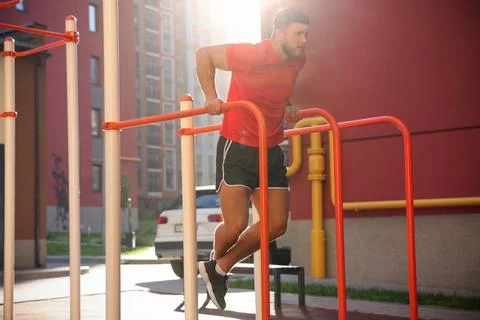 Man training on parallel bars at outdoor gym on sunny day Stock Photos