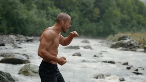 Man is training punches on river shore, workout in nature, force of human and 库存影片 163330979