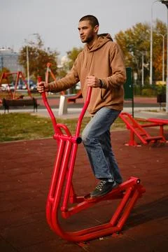 Man training on red stepper machine in outdoor gym, autumn city park. The Stock Photos