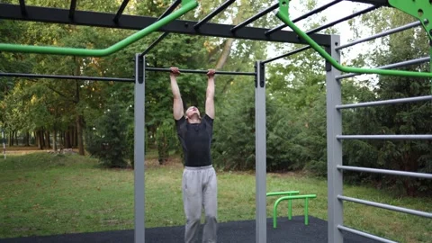 Man trains outdoors performing dynamic pull up exercise on modern green metal ba Video stock 316701772