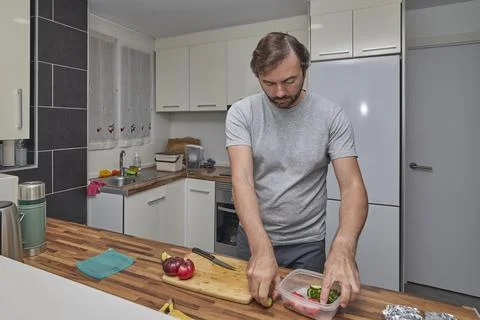 A man transfers cut vegetables into a plastic container Stock Photos