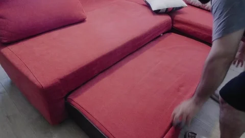A man transforms a red sofa into a bed by pulling out the mattress and Stock Footage 342665930
