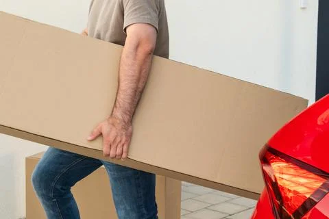 Man transporting large cardboard box from car to home in residential setting Stock Photos