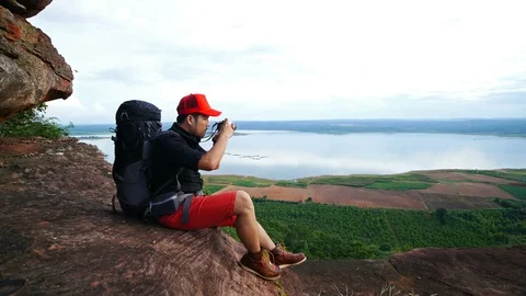 Man traveler with backpack using camera taking a photo on the edge of cliff Stock-Footage 128215926