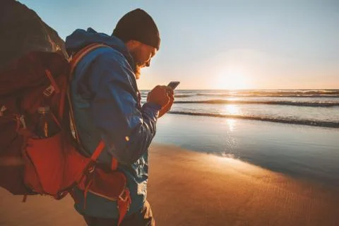 Man traveling with backpack using smartphone on beach navigation application  Stock Photos