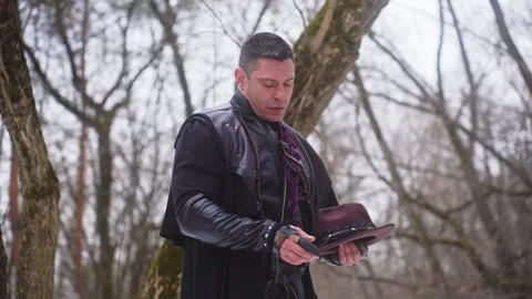 Man by tree in forest holding hat, surrounded by natural landscape Video stock 270485656