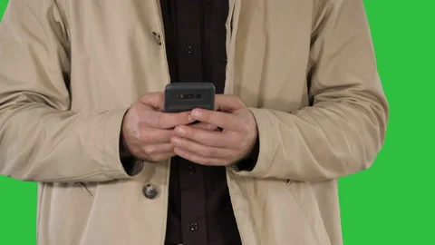 Man in trench coat using mobile smart phone on a Green Screen, Chroma Key. Stock Footage 100569905