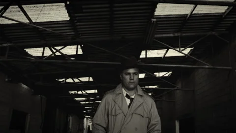 Man in trench coat walking through factory hallway in black and white Video stock 275643624