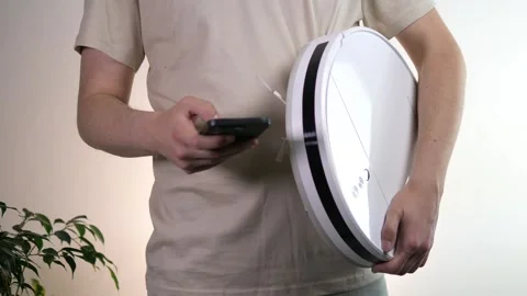 A man tries to connect a robot vacuum cleaner to his phone and set it up Stock Footage 312797075