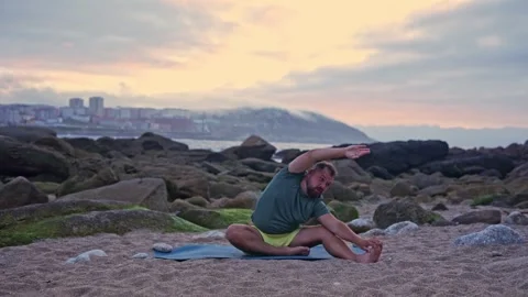 A man tries to do yoga for the first time, pulls his hand to the side, doing Stock Footage 242347313