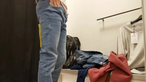 A man tries on jeans in front of a mirror in a boutique fitting room Stock Footage 301780917
