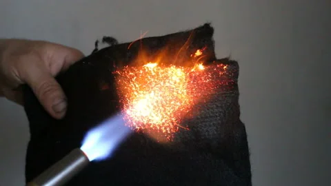 A man tries to set fire to a black refractory fabric with a gas burner. Real tim Stock Footage 131821763