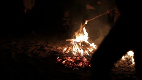 Man tries to spread a dying fire with a stick, sparks fly from the firewood Stock Footage 115930053