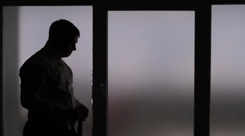 A man tries on a tie against the window. The silhouette of a man. Stock Footage 65331615