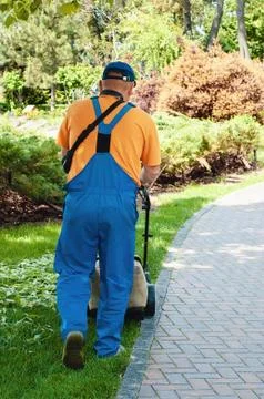 Man trimming fresh grass using brush cutter in a summer park Stock Photos