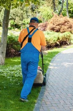 Man trimming fresh grass using brush cutter in a summer park Stock Photos