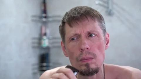 Man trims his beard with an electric razor in the bathroom Stock Footage 275963200